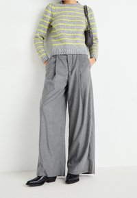 Harmaa raidallinen neule neonkeltaisilla viivoilla, yhdistetty leveälahkeisiin harmaisiin housuihin. Asun täydentävät mustat korolliset kengät.