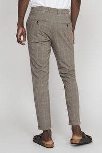 Svijetlosmeđi karirani hlače slim fit kroja, sužene nogavice i s preklopljenim rubovima, koje imaju dva stražnja džepa s dugmadima. Crne sandale na sklizak.