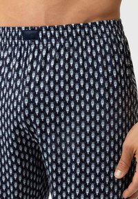 Marineblauwe boxers met een patroon en een zachte elastische tailleband, voorzien van kleine lichtblauwe en witte ontwerpen van tekenfilmfiguren.