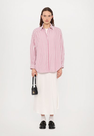 Chemise oversize rayée rose et blanche, jupe midi blanche, sac à main noir et chaussures noires à boucle avec des chaussettes blanches. Texture de tissu lisse.