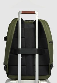 Mochila de tela verde con interior acolchado negro, con un asa telescópica y detalles de cuero. Dos correas laterales para mayor estabilidad.