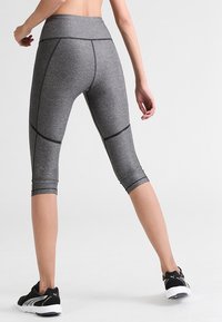 Szare legginsy capri o dopasowanym kroju, z czarnymi akcentami i szwami, wykonane z teksturowanego, elastycznego materiału. Stylizowane z czarnymi trampkami.