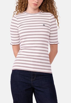 Femme portant un t-shirt blanc côtelé à manches courtes avec de fines rayures horizontales marron rouge et un jean bleu foncé.