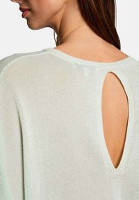 Top de punto verde claro con escote en forma de llave en la espalda, corte relajado y textura suave con un ligero brillo.