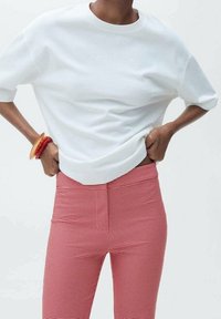 Witte katoenen top met korte mouwen, gecombineerd met hoogwaistbroeken in een rood-wit houndstooth patroon. Soepele textuur, getailleerde silhoutte.