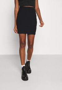 Mini gonna nera a coste con silhouette aderente. Abbinata a stivali neri alla caviglia e calze bianche per creare contrasto. Design minimalista.
