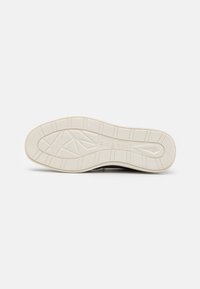 Semelle d'une chaussure présentant un fond en caoutchouc blanc texturé et à motif, avec des rainures angulaires et le logo "bugatti" en relief.