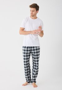 Biela krátkorpíšová tričko v kombinácii s čierno-bielymi károvanými pyžamovými nohavicami, so voľným strihom a mäkkou textúrou. Postoj naboso.
