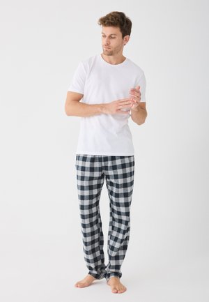 Vit kortärmad t-shirt i kombination med svart och vit rutiga pyjamasbyxor, med en avslappnad passform och mjuk textur. Barfota hållning.