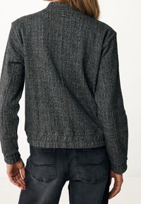 Veste à motif pied-de-poule en noir et blanc, avec un design ajusté, des poignets côtelés et une taille élastique. Associée à un jean gris foncé.