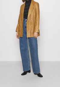 Brun læder dobbeltradet blazer med sølvknapper, parret med højtaljede blå vide jeans og sorte spidse ankelstøvler.