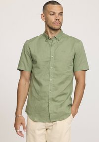 Chemise à manches courtes, à boutonner, en tissu vert clair, avec une texture lisse, des coutures discrètes et un petit logo brodé sur la poitrine.