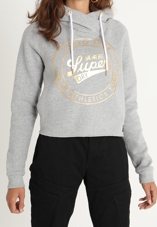 Grijze cropped hoodie met een gouden logo-opdruk, voorzien van een capuchon met trekkoord en geribbelde manchetten, gecombineerd met zwarte cargo-broeken.