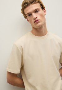 T-shirt beige a maniche corte realizzato in tessuto morbido, con scollatura rotonda e design minimalista senza motivi o dettagli.