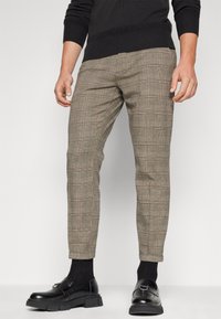 Brown plaid trousers with a slim fit, featuring a texture blend and rolled cuffs. Paired with black loafers and dark socks.