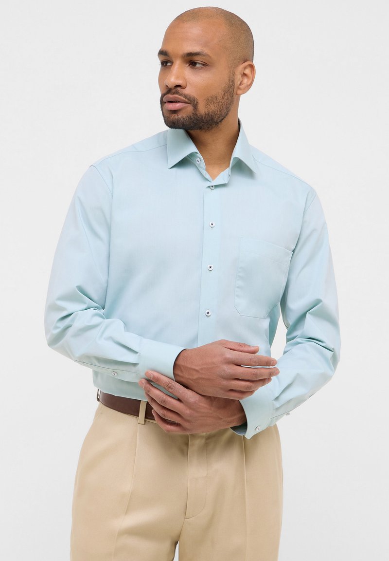 Lichtblauw long-sleeve shirt met een puntige kraag, voorzak en knoopsluiting. Gemaakt van gladde stof, gecombineerd met beige broek.