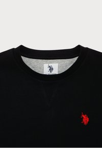 T-shirt noir col rond avec petit logo brodé rouge d’un joueur de polo sur la poitrine et doublure intérieure grise du col avec étiquette de marque visible.