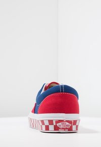 Rode en blauwe canvas sneaker met een geblokte witte rubberen zool. Heeft een ronde neus en een logo-label achteraan. Zichtbare stiksels op de bovenkant.