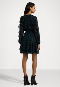 Grønn ruter kjole med lange volangermer, innsnevret midje og lagdelt skjørt, komplettert med svarte ankelstøvletter.