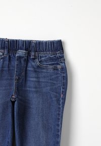 Dark blue denim jeans featuring an elastic waistband, two front pockets, and decorative stitching along the seams. Smooth texture, straight leg design.