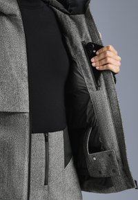 Kabát so vzorom houndstooth v šedej farbe s čiernym interiérom, obsahujúci vrecká na zips a textúrovaný povrch.