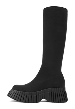 Svart knäkänga i texturerat tyg, med en tjock kilar sål med vertikal ribbning och en rundad tådesign.