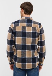 Plaid flannel shirt in beige, navy, and light blue with a button-down collar and long sleeves, featuring a back yoke and rounded hem.
