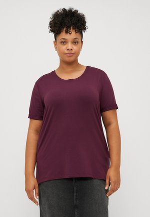 T-shirt bordeaux à manches courtes avec un col rond, fabriqué en tissu doux. Présente des poignets roulés et une coupe décontractée, associé à une jupe gris foncé.