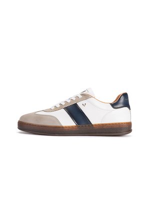 Baskets blanches avec un bout en daim beige, une bande latérale bleu foncé, des lacets blancs et une semelle marron avec un aspect légèrement usé.