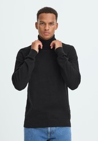 Schwarzer Rollkragenpullover aus weichem Strickstoff, mit langen Ärmeln, tailliertem Schnitt und gerippten Akzenten am Kragen und Saum.