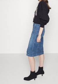 Ljusblå denimpennkjol med rå fåll, tillsammans med en svart sweatshirt med metallicdetaljer och kraftiga svarta klackstövlar.