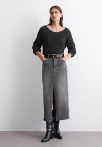 Chunky gray knit sweater with wide neckline, paired with a long gray denim skirt featuring a front slit. Black belt and knee-high black boots.