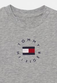 Grå bomullströja med en rund logotyp som har texten "TOMMY HILFIGER" och ett rektangulärt emblem i röd, vit och blå färg.