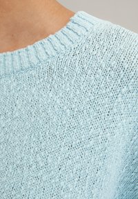 Hellesblau gestrickter Pullover mit geripptem Halsausschnitt, strukturierter Textur und kleinen gemusterten Details überall.