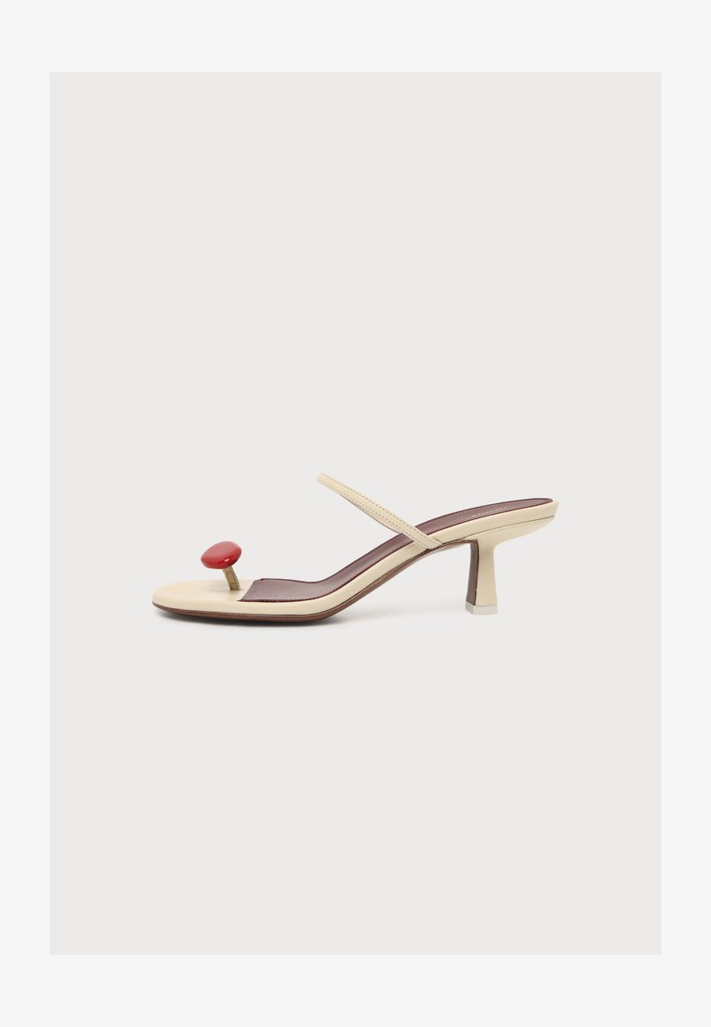 Sandale à talon beige avec une fine bride et un séparateur d'orteil rouge circulaire sur fond blanc.