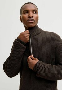 Strickpullover in Dunkelbraun mit hohem Kragen und durchgehendem Reißverschluss, der mit einer strukturierten Rippstruktur und übergroßen Ärmeln versehen ist und ein strukturiertes Design betont.