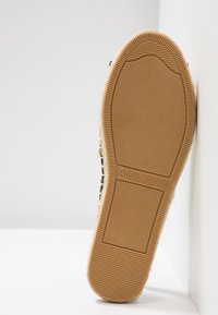 Vue inférieure d'une semelle en caoutchouc beige avec une adhérence texturée et le numéro de pointure 4 sur une chaussure décontractée sur un fond blanc.