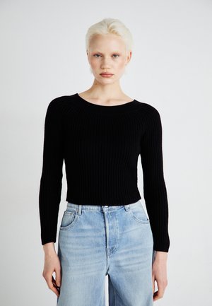 Svart ribbet langermet genser med bred hals, paret med lyseblå høy midje denimbukser. Teksturen på stoffet er synlig.