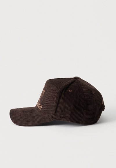 Casquette de baseball en velours côtelé brun foncé avec une visière courbée, logo brodé et texte sur le panneau avant, vue de côté gauche sur fond blanc.