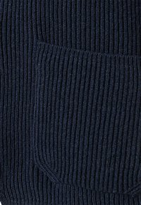 Navy ribbed knit fabric featuring a pocket with a rounded corner, showcasing a textured and layered appearance throughout.