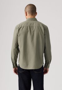 Πουκάμισο σε ελιά πράσινο με κουμπιά, μακριά μανίκια, ραφή γιόκ πίσω και μανσέτες με διακοσμητικά κουμπιά, κατασκευασμένο από ελαφρύ ύφασμα.