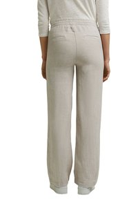 Femme portant un pantalon beige à jambes larges avec une taille élastique et des poches fendues à l'arrière, associé à des baskets blanches et une chemise légère à manches longues.