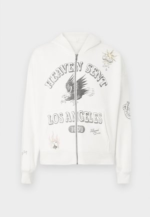 Bijela dukserica sa zipom s grafičkim natpisom "HEAVEN SENT LOS ANGELES 1971", dizajnom orla i dekorativnim aplikacijama uključujući sunce i igraću kartu.