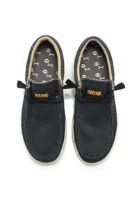 Zapatos slip-on de malla negra con acentos beige y suelas de goma. El interior presenta un forro gris con un patrón de calaveras y huesos cruzados en blanco.