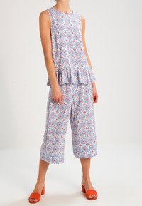 Ensemble composé d'un haut à motif multicolore et de pantalons courts, avec un ourlet volanté, dans des tons de bleu, rouge et blanc ; associé à des sandales orange.