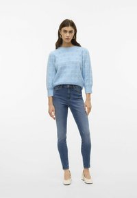 Pull en mailles texturé bleu clair à manches longues, associé à un jean bleu ajusté et des chaussures à talons couleur crème.