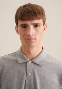 Polo grigio con colletto classico e allaccio a due bottoni. La trama del tessuto appare morbida, con una superficie liscia ed uniforme.