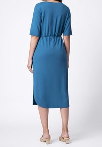 Niebieska sukienka z luźnym krojem, krótkimi rękawami, ściągniętym w pasie, z bocznymi rozcięciami i zaokrąglonym dołem, w połączeniu z beżowymi sandałami na koturnie.