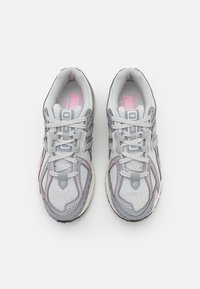 Un paio di scarpe da corsa New Balance grigie e rosa con lacci, viste dall'alto su uno sfondo bianco.