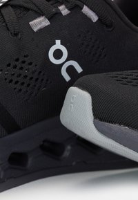 Schwarze Laufschuhe mit atmungsaktivem Mesh-Obermaterial, grauen Akzenten, strukturierten Sohlen und einem markanten, wolkenartigen Dämpfungsdesign.